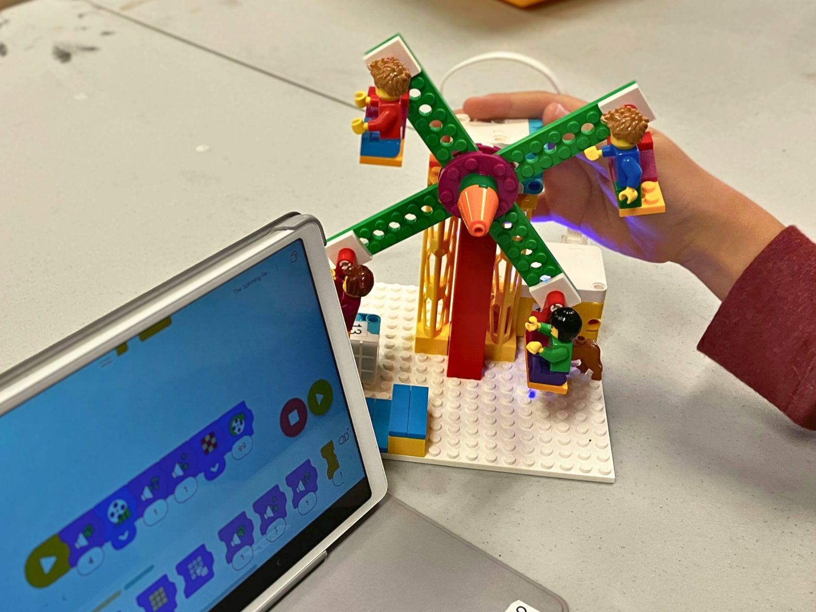 A child holds a LEGO ferris wheel model next to a tablet showing its code