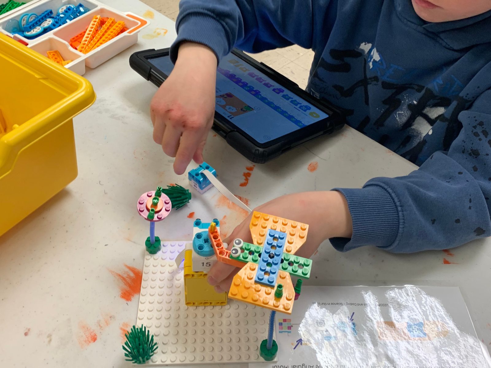 A child builds a LEGO windmill while coding on a tablet