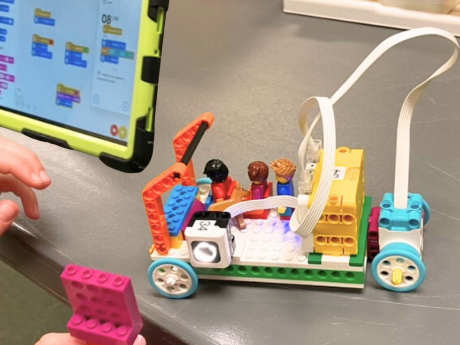 A LEGO vehicle with minifigures next to a coding tablet